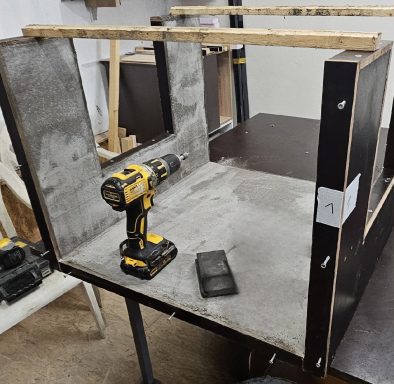 Ein Holzgestell mit Betonflächen und einem Akku-Bohrer auf einem Arbeitstisch.