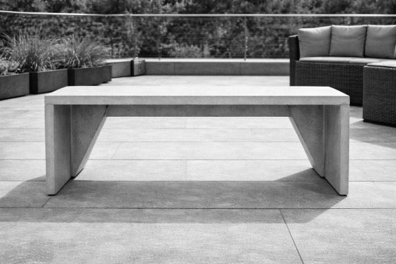 Eine moderne, minimalistische Sitzbank aus Beton auf einer Terrasse.