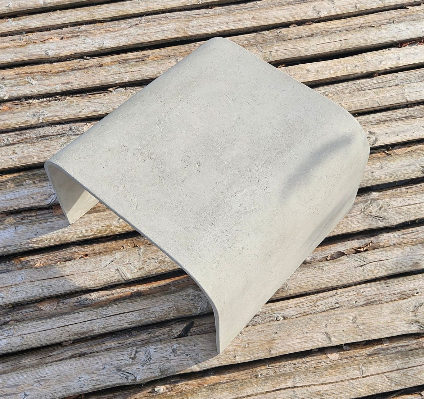 Tavolo Grezzo Graues, gewölbtes Objekt auf einem Holzuntergrund.